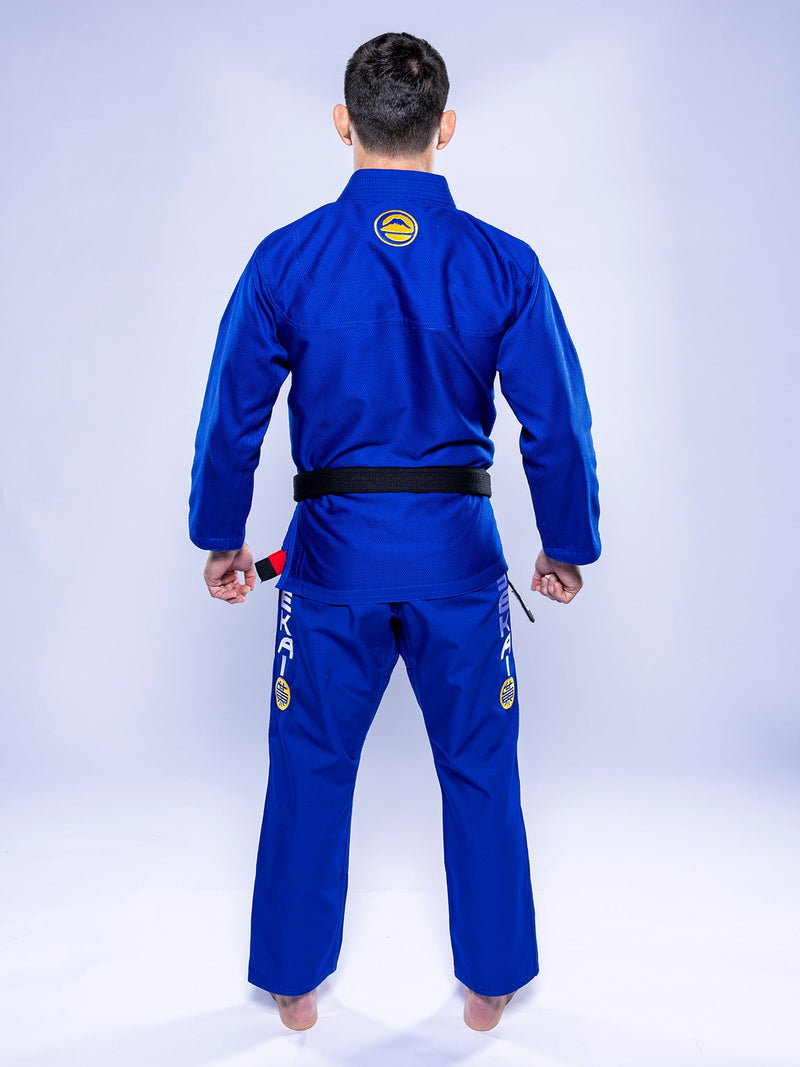 A person stands barefoot, back to the camera, wearing the SEKAI 3.0 BJJ Gi Blue Yellow with patches and a black belt against a light background.