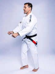 A man stands barefoot on a light background, side-on with arms bent as if preparing for movement, wearing the SEKAI 3.0 BJJ Gi White Navy and a black belt.
