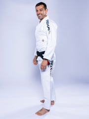 A man wearing the SEKAI 3.0 BJJ Gi White Navy with dark lettering on the sleeve and pants stands barefoot on a white background, smiling and looking at the camera.