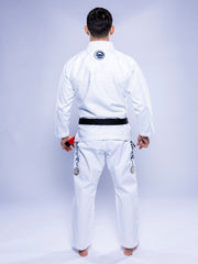 A person stands barefoot, facing away in the SEKAI 3.0 BJJ Gi White Navy with a black belt. The gi features patches on sleeves and pants, set against a plain light-colored background.