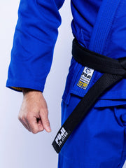 A person wearing the SEKAI 3.0 BJJ Gi Blue Yellow with a black belt labeled “FUJI JIU JITSU,” showing their fist and part of their torso.