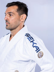 A man with short dark hair and a trimmed beard wears the white-navy SEKAI 3.0 BJJ Gi, embroidered with "SEKAI" on the shoulder, looking left against a plain light background.