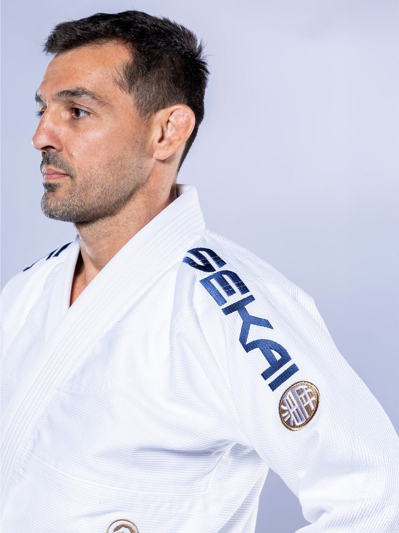 A man with short dark hair and a trimmed beard wears the white-navy SEKAI 3.0 BJJ Gi, embroidered with "SEKAI" on the shoulder, looking left against a plain light background.