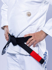 A person wearing the SEKAI 3.0 BJJ Gi White Navy with a black belt featuring a red bar stands confidently with hands on hips, displaying the securely tied belt around their waist.