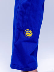 A close-up of someone wearing the SEKAI 3.0 BJJ Gi Blue Yellow, featuring a yellow circular mountain patch on the upper leg. The background is light and uncluttered.