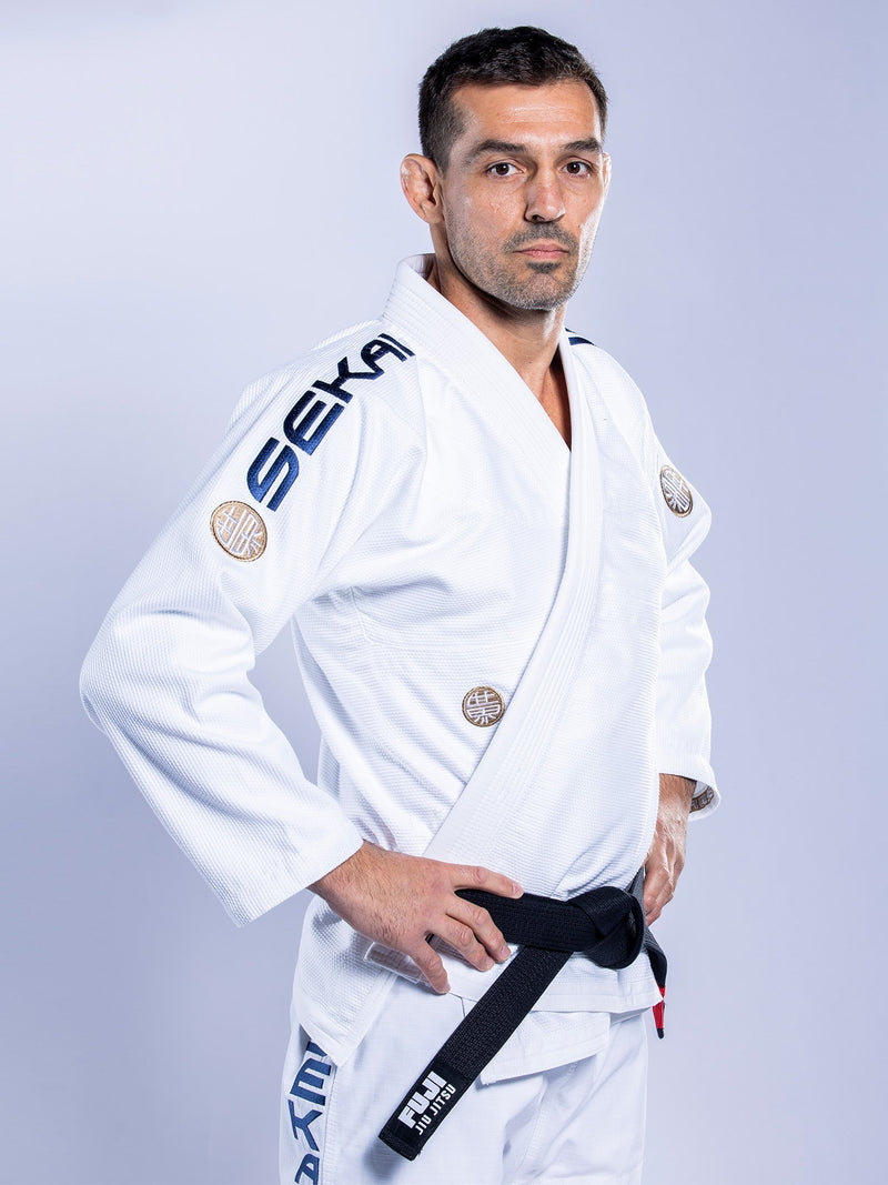 A man stands confidently with hands on hips, wearing the SEKAI 3.0 BJJ Gi White Navy and a black belt, looking at the camera against a plain light background.