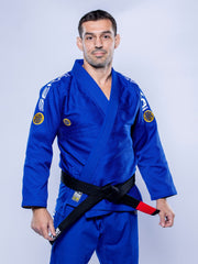 A man in the SEKAI 3.0 BJJ Gi Blue Yellow with a black belt stands confidently against a light grey background.