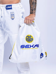 A person in white SEKAI 3.0 BJJ Gi (White Navy) holds a white drawstring bag labeled SEKAI WORLD RANKING with blue, yellow accents, and Japanese characters against a light background.