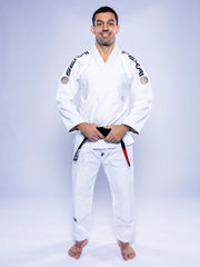 A man wearing the SEKAI 3.0 BJJ Gi White Navy with a black belt stands barefoot on a white background, smiling and facing forward with his hands resting on his belt.