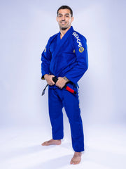 A man stands barefoot on a white background, smiling while wearing the SEKAI 3.0 BJJ Gi Blue Yellow with patches and holding his black belt tied around his waist.