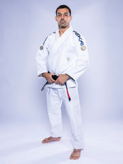 A man stands barefoot on a white background, wearing the SEKAI 3.0 BJJ Gi White Navy with a black belt. He faces forward, confidently holding his belt and looking at the camera.