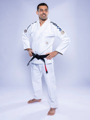 A man stands barefoot on a plain light background, smiling with his hands on his hips and wearing the SEKAI 3.0 BJJ Gi White Navy with a black belt.