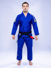 A man stands barefoot on a white background, wearing the SEKAI 3.0 BJJ Gi Blue Yellow with a black belt, facing forward and arms relaxed at his sides.